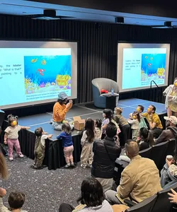 Karla interacting with a group of children during a storytelling performance. An animated underwater and fun scene is projected on screens behind her.