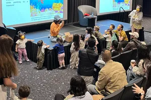 Karla interacting with a group of children during a storytelling performance. An animated underwater and fun scene is projected on screens behind her.